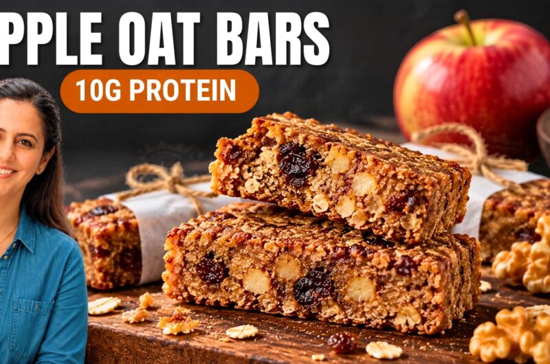 Stack of high protein apple oatmeal bars with walnuts and raisins on a wooden board, with a red apple behind